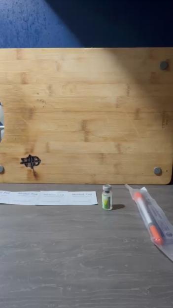 Items for a peptide injection, including alcohol pads, a vial, and a syringe package, on a grey table in front of a wooden board.