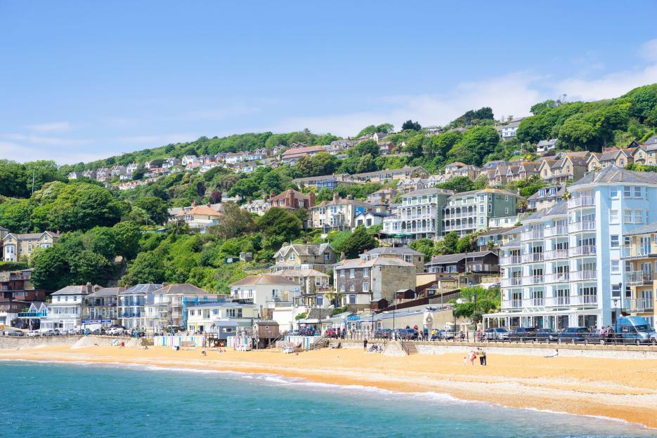 View of a hillside town with houses and buildings leading down to a sandy beach and blue ocean.