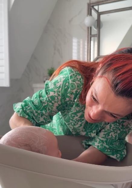 Dianne Buswell leaning over a baby bath, looking at the baby being bathed.