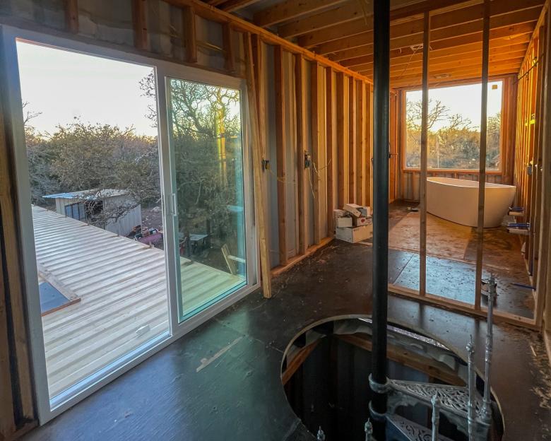 Framing, wiring, and a spiral staircase installed in a shipping container home under construction.