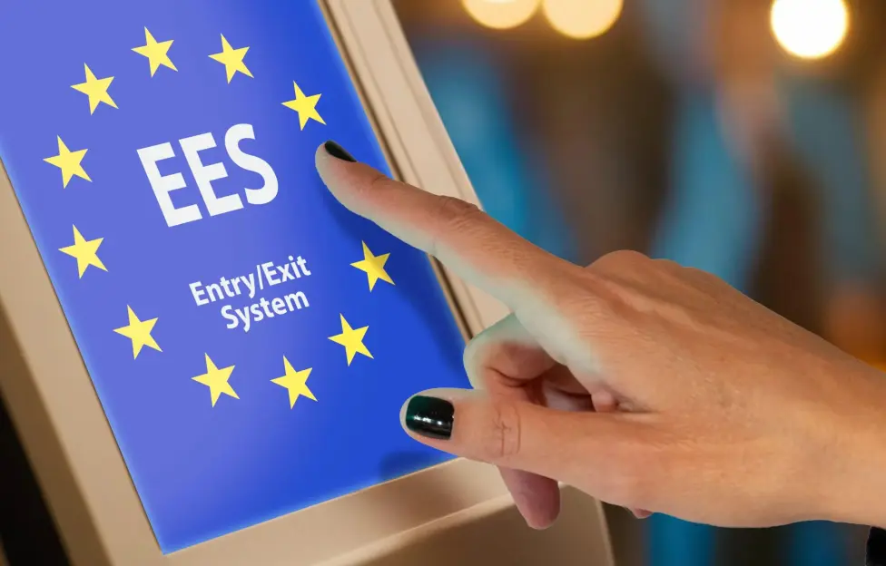 Woman's hand touching a screen displaying "EES Entry/Exit System" on a European Union flag background.