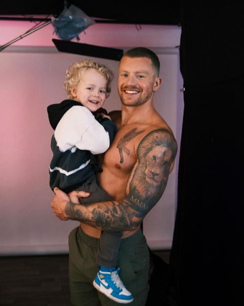 Adam Peaty holding his son, George, both smiling at the camera.