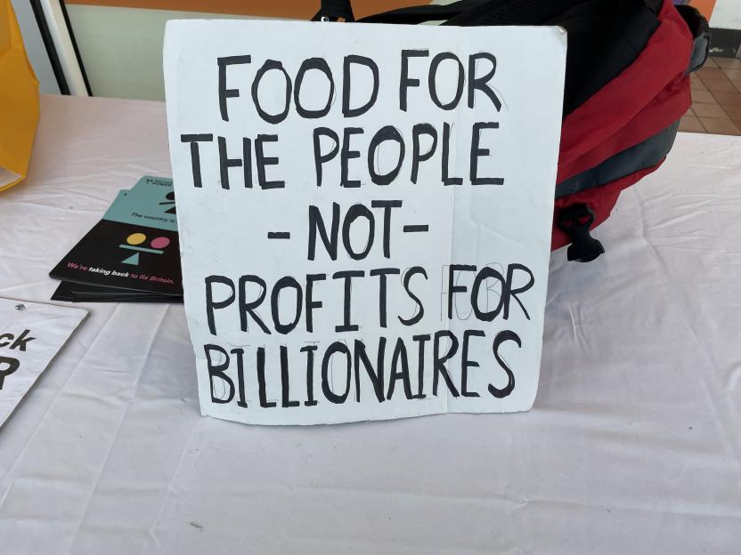 A protest sign reads "FOOD FOR THE PEOPLE - NOT - PROFITS FOR BILLIONAIRES."