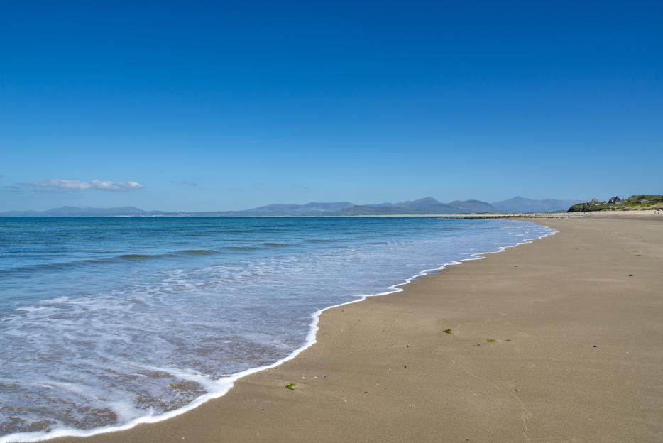 Llandanwg beach with blue water and sky, and mountains in the distance.