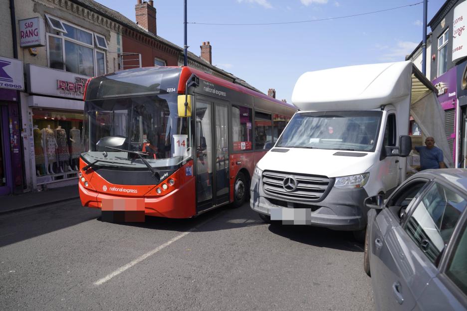 A red National Express bus blocked by a white Mercedes van and a gray car on Alum Rock Road due to bad parking.