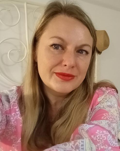 A woman with long blonde hair and red lipstick smiles into the camera.