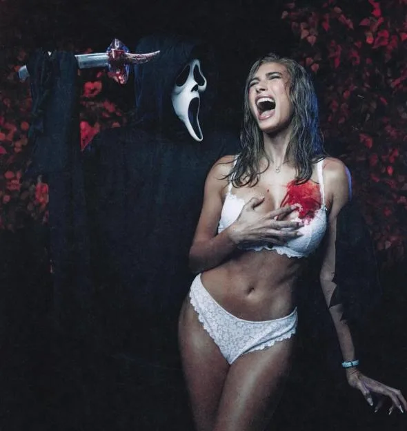 Hailey Bieber in white lingerie and fake blood screams as the Ghostface killer holds a bloody knife behind her in a recreation of Scary Movie.