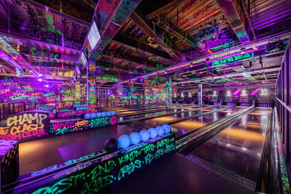 A neon-lit bowling alley featuring graffiti-covered walls and lanes.