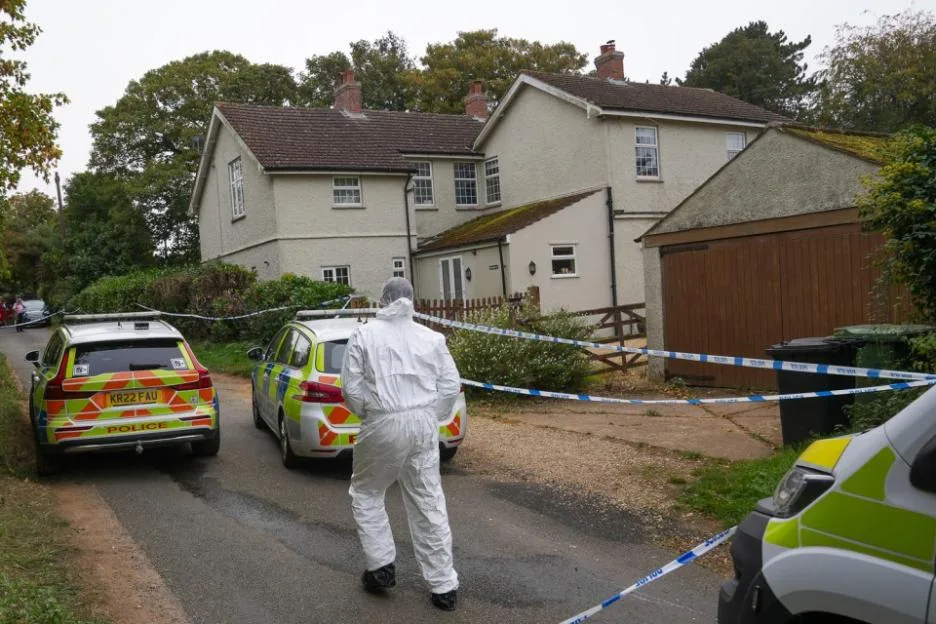 Police cars and a forensic investigator in a protective suit outside a house in Dersingham, Norfolk.