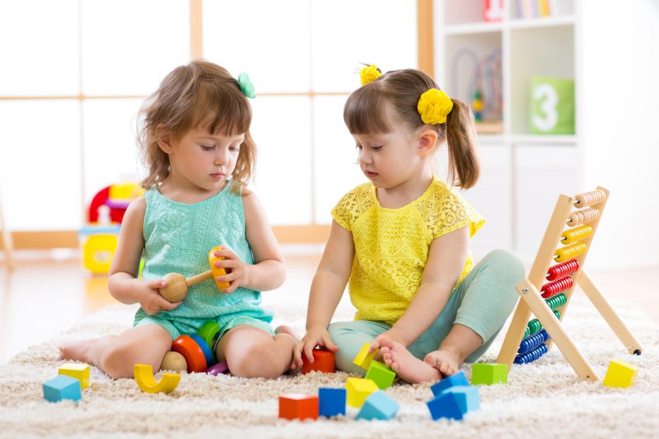 Two young girls playing together on a rug with building blocks and an abacus.