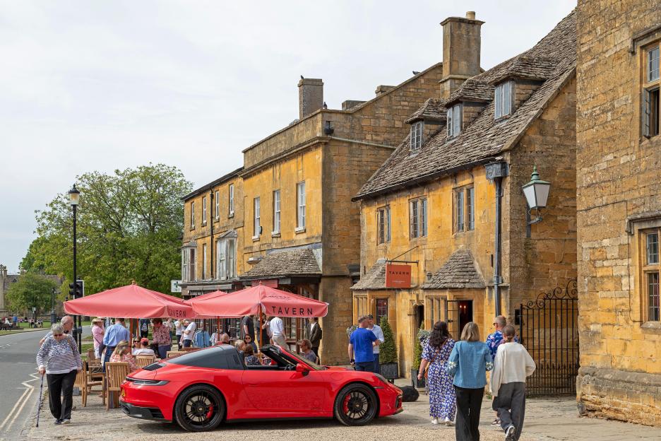 Honey colored houses, cottages, a pavement cafe, and a red sports car on High Street, Broadway, Worcestershire, The Cotswolds, England, Great Britain.