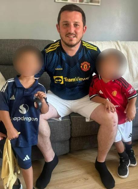 A man in a Manchester United jersey sitting on a sofa with two children, their faces blurred out.