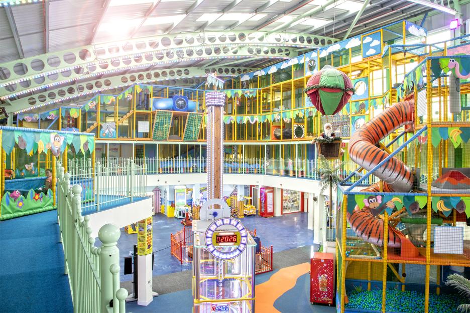 An indoor adventure park called Adventure Inside Essex, with colorful jungle-themed play structures, a large tiger slide, a drop tower ride, and arcade games.