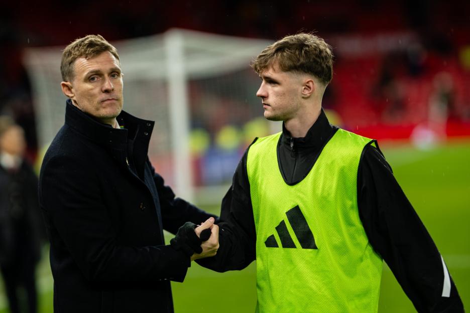 A coach in a dark coat shakes hands with a young player in a neon green vest.