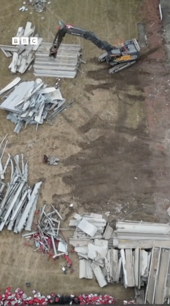 Aerial view of a demolition site with a large excavator moving debris.