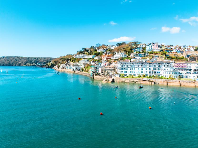 Drone view of the Salcombe coastline with colorful homes and boats in the water.