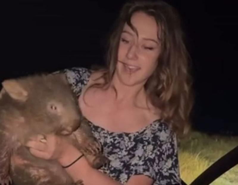 A young woman holding a wombat at night.