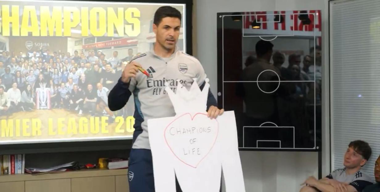 Mikel Arteta holds a paper cut-out of the Premier League trophy with "Champions of Life" written on it.