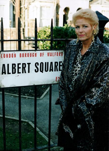 A woman stands in front of a sign for Albert Square.