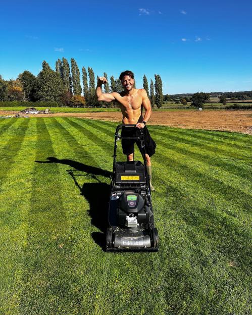 Mark Wright posing shirtless while mowing his lawn, flexing his biceps.