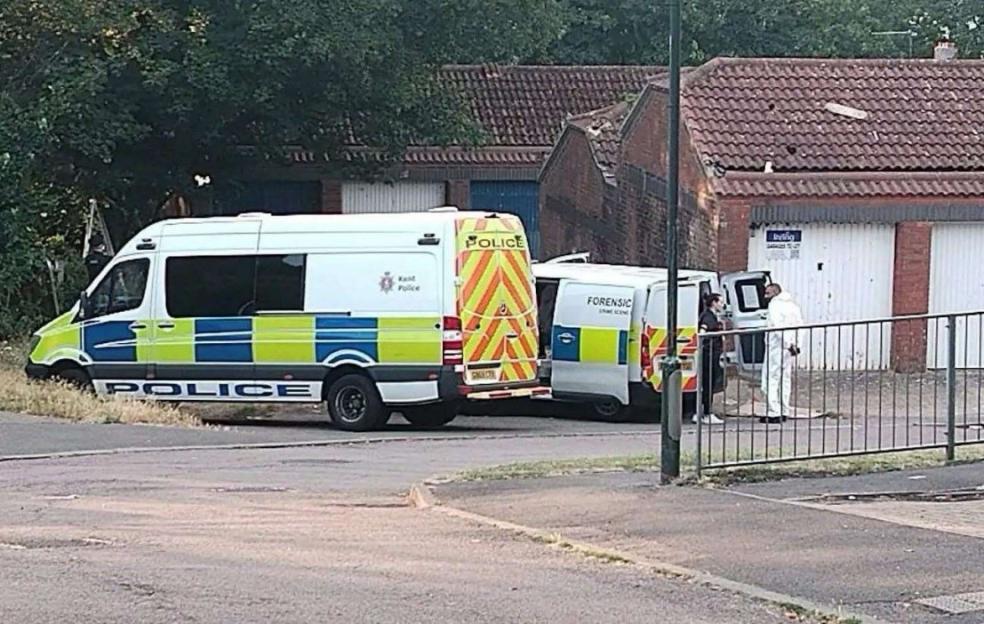 Police and forensic vans at a park near garages.