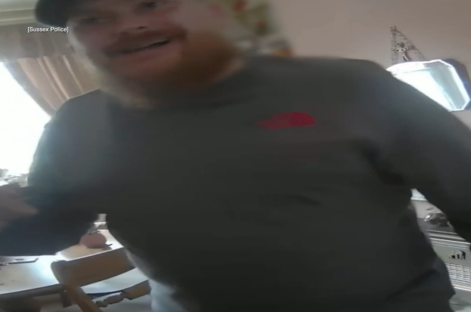 A man in a baseball cap and grey shirt, with a red hat logo, captured from a body camera's point of view.