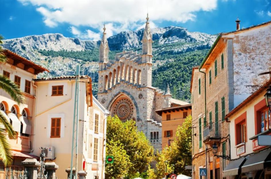 A large stone church with a circular stained-glass window in a town with mountains in the background.