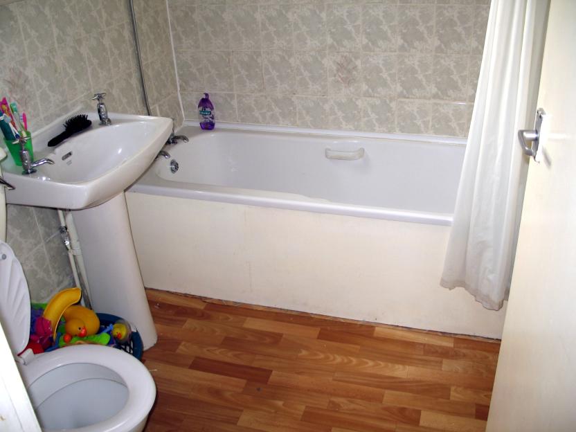A bathroom with a white bathtub, sink, toilet, and wooden floor.