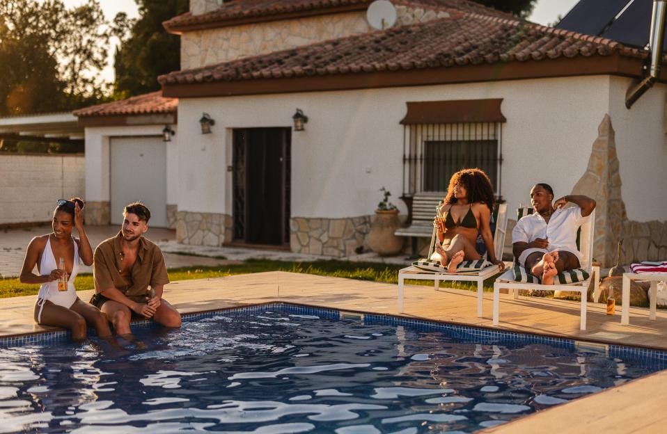 Four friends enjoying drinks by the pool during summer vacation.