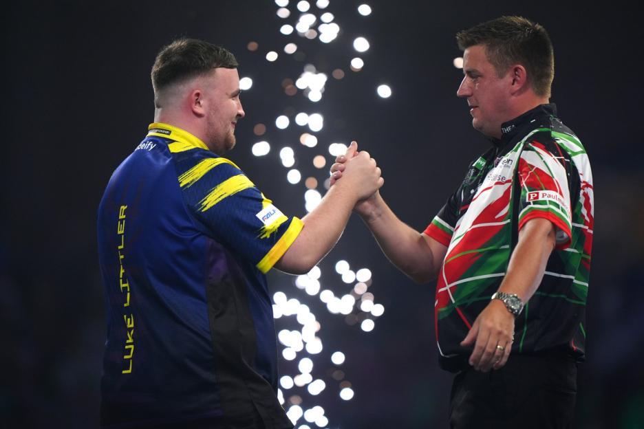 Two darts players, Luke Littler and another, shaking hands on stage with bright lights in the background.