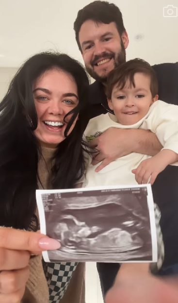 A family of three, with the mother holding up a sonogram.