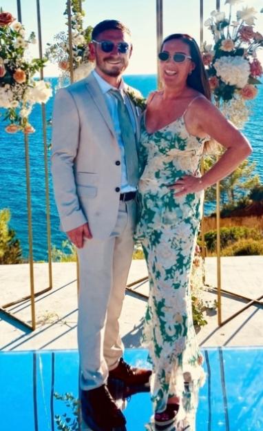 A couple smiling with floral arrangements and the ocean in the background.