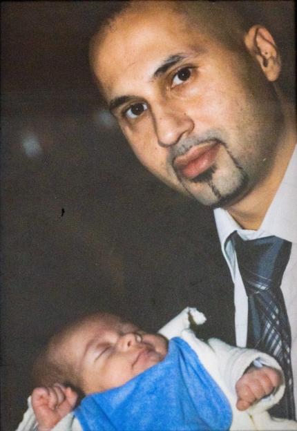 A man with a goatee wearing a shirt and tie holds a sleeping baby.