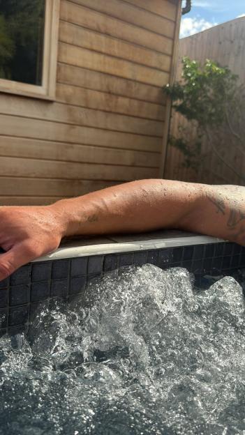 A man's wet arm, tattooed with the name "Chloe", resting on the edge of a hot tub.