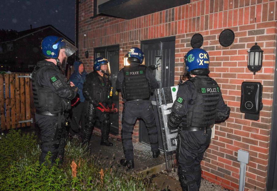 Police officers in riot gear raid a building.