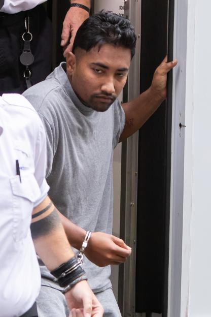 Moynul Janu, in handcuffs and a grey t-shirt, is escorted by security staff.