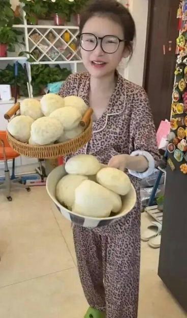 A young woman in leopard print pajamas and glasses holds a basket and a bowl filled with steamed buns.