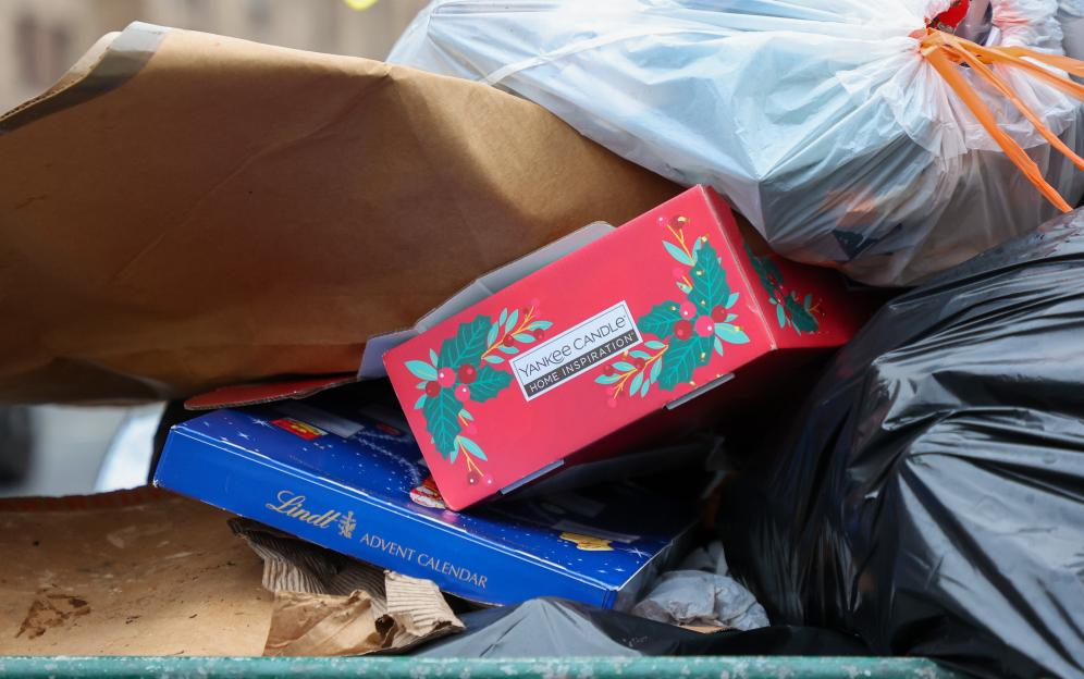 A pile of garbage bags overflowing with a red Yankee Candle box and a blue Lindt Advent Calendar box.