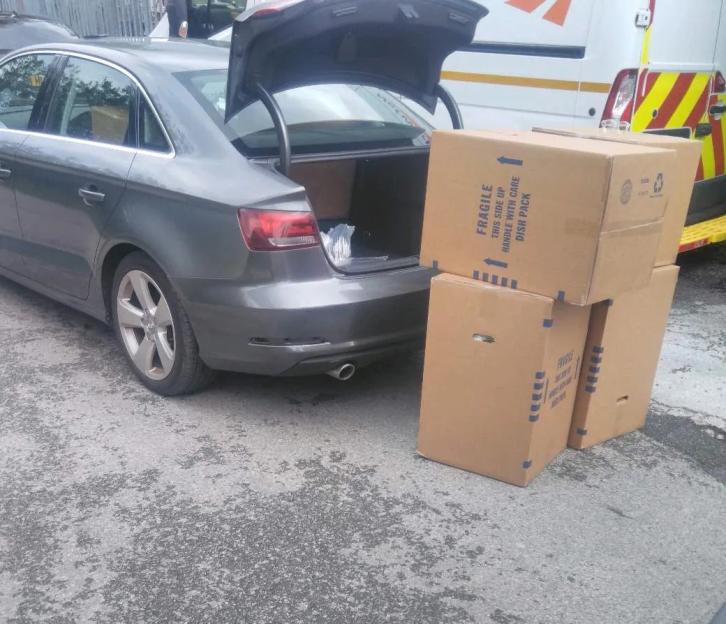 Several boxes, some labeled "fragile," sit next to a car with an open trunk.