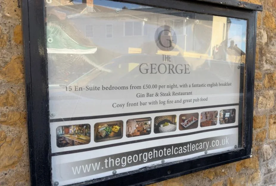 A sign for the George Hotel in Castle Cary, featuring details about its rooms, restaurant, and bar.