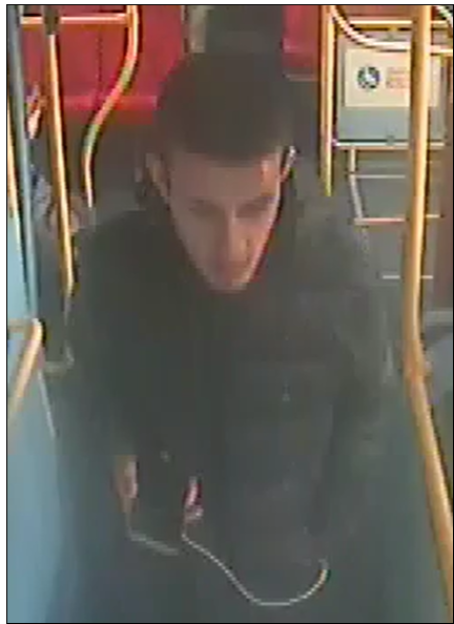 Security camera footage of a man in a black jacket and hoodie on a bus.