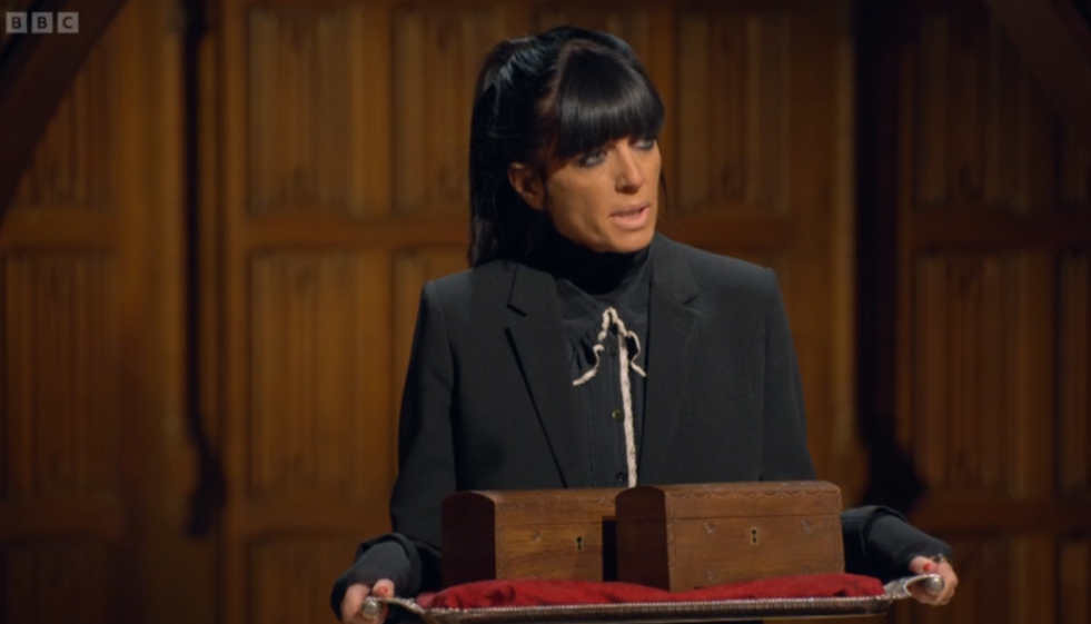 A woman in a black suit holds a tray with two wooden boxes.