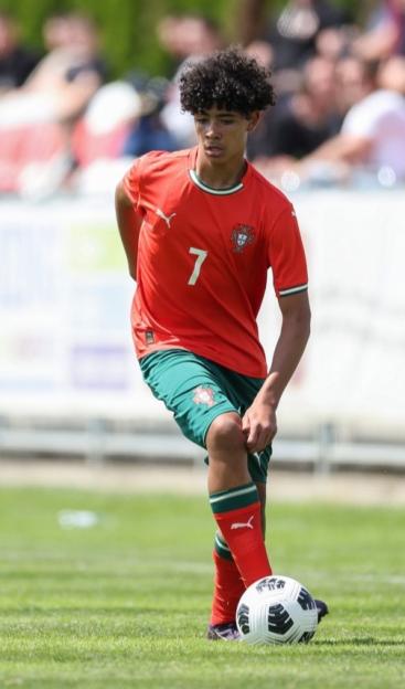 Cristiano Jr. in a red and green uniform playing soccer against Japan.