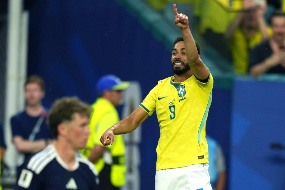 A Brazilian soccer player in a yellow jersey raises his arm and points his finger.