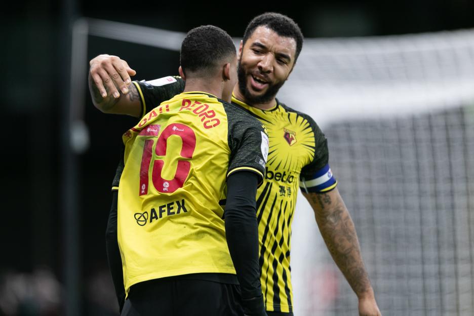 Two male footballers in yellow and black striped jerseys celebrating on the field.