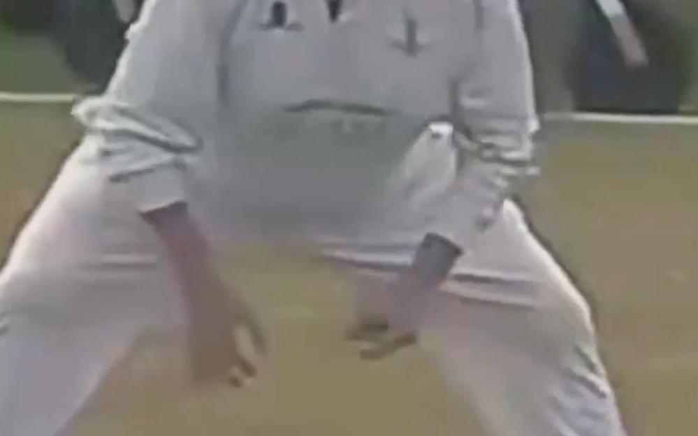 A blurry photo of a person wearing white clothing, squatting with their hands near their knees.