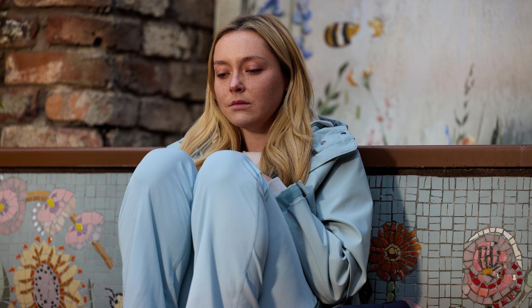 Megan, dressed in blue, sits looking distraught in Victoria Garden.