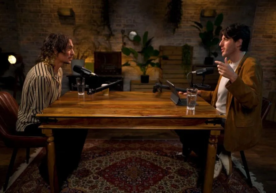 Two men at a wooden table with microphones for a podcast recording.