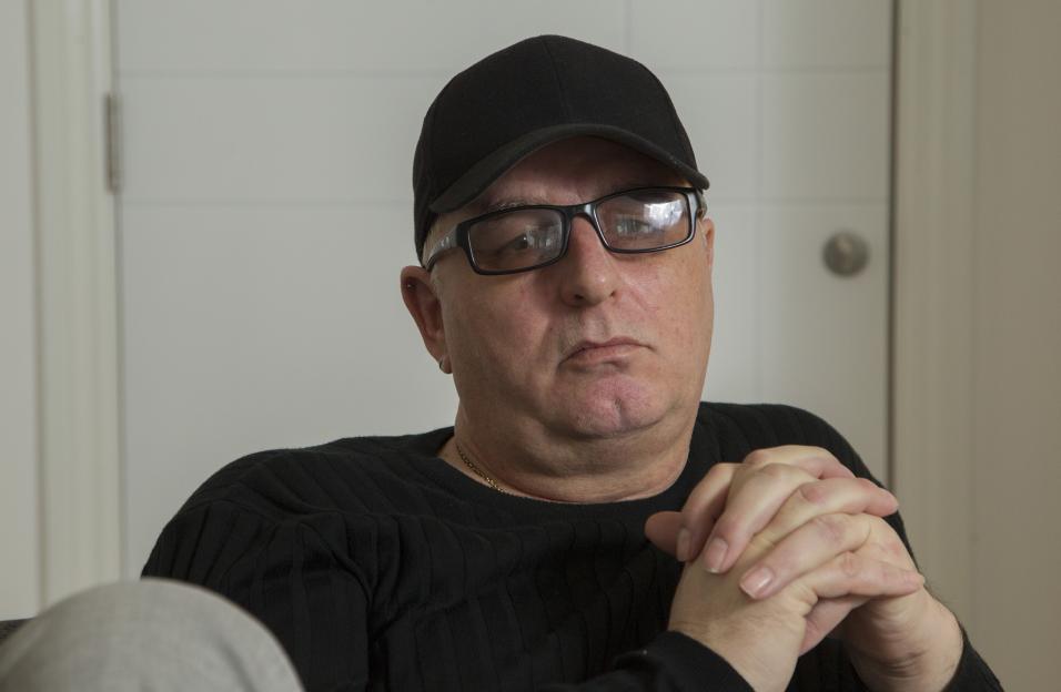Andros Georgiou wearing a black cap and glasses, with hands clasped together.