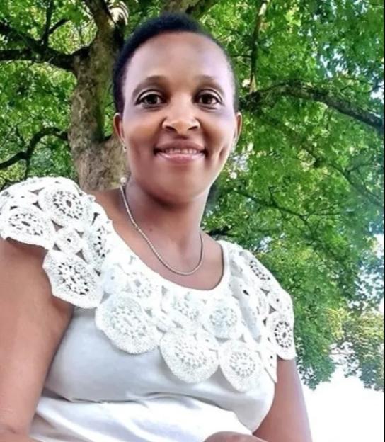 A smiling woman in a white lace top with a tree in the background.